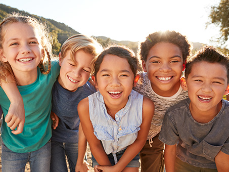A group of kids with arms around each other's shoulders smiling on a sunny day