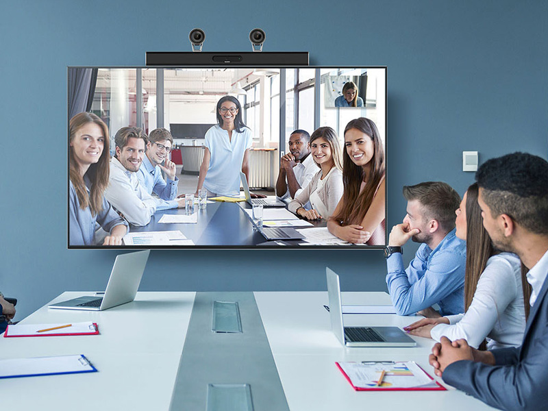 A group of young professionals in an office and on a TV screen participating in a Huawei telepresence video conference