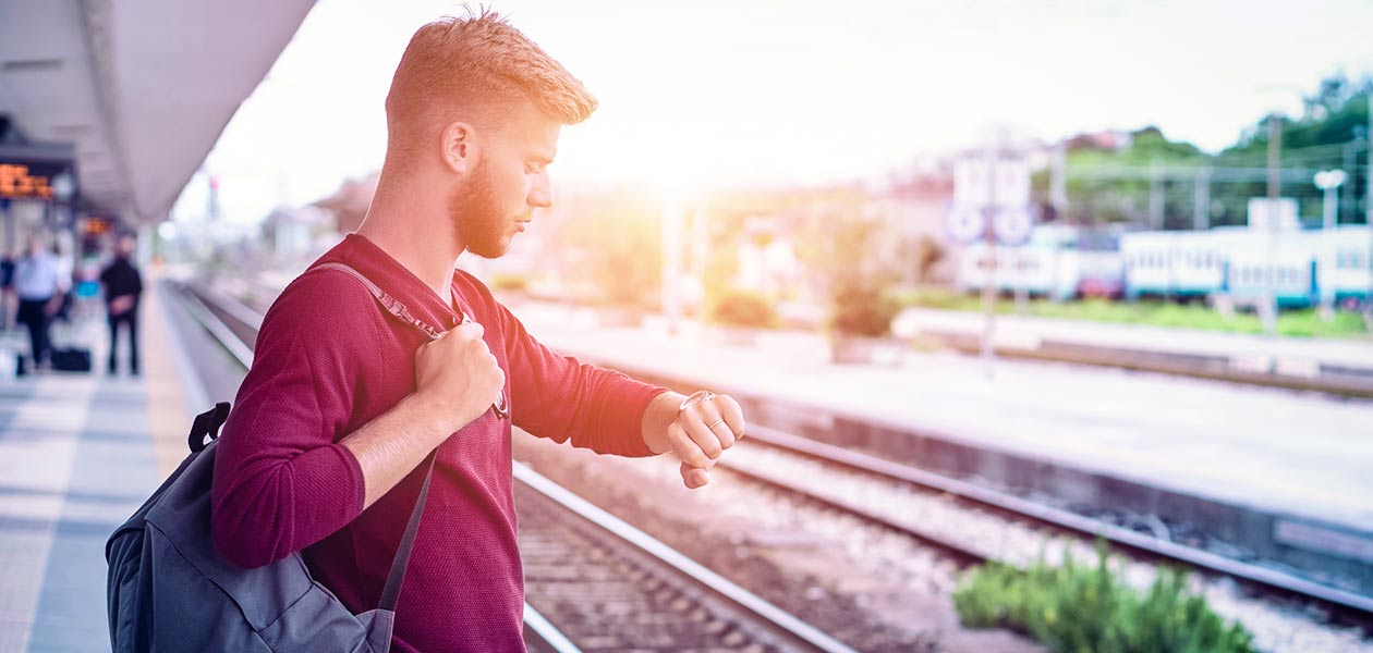 A man looks at his watch standing on a train station platform, backlit by the sun, illustrating Huawei FTTM for stations